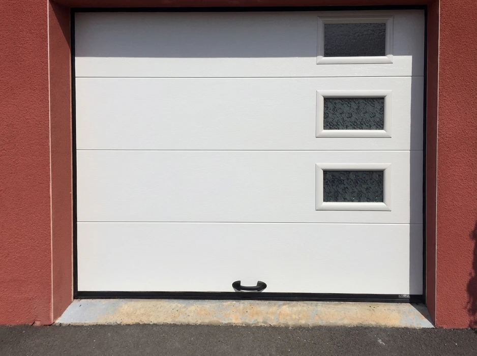 Porte de garage sectionnelle blanche, installation extérieure, encadrée de piliers en stuc rouge
