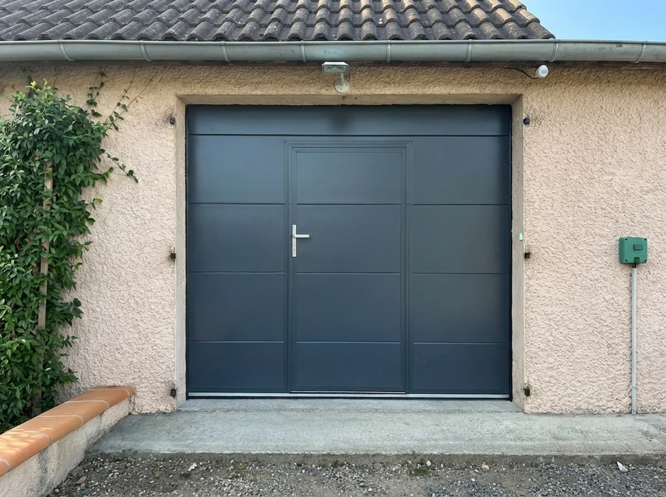 Façade extérieure d'un garage résidentiel avec porte sectionnelle coulissante grise anthracite (RAL 7016), intégrant une porte piétonne avec poignée en inox brossé