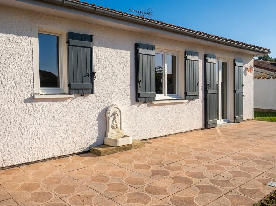 Façade extérieure d'une maison de plain-pied, crépi blanc, volets battants gris anthracite sur fenêtres PVC blanches à double vitrage