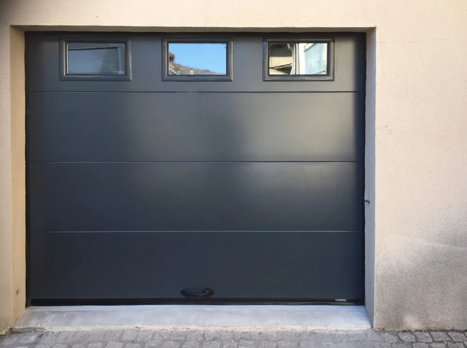 Porte de garage sectionnelle, finition lisse, coloris anthracite RAL 7016, avec bandeau vitré composé de trois hublots rectangulaires en partie haute