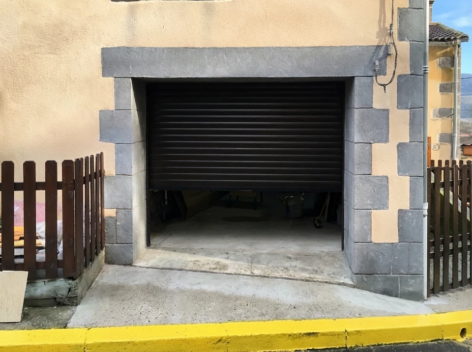 Garage résidentiel moderne en soirée avec porte sectionnelle en cours d'ouverture révélant une voiture blanche garée à l'intérieur