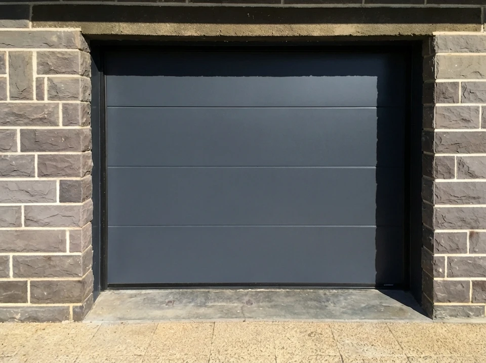 Porte de garage sectionnelle, finition lisse, coloris anthracite RAL 7016, avec bandeau vitré composé de trois hublots rectangulaires en partie haute