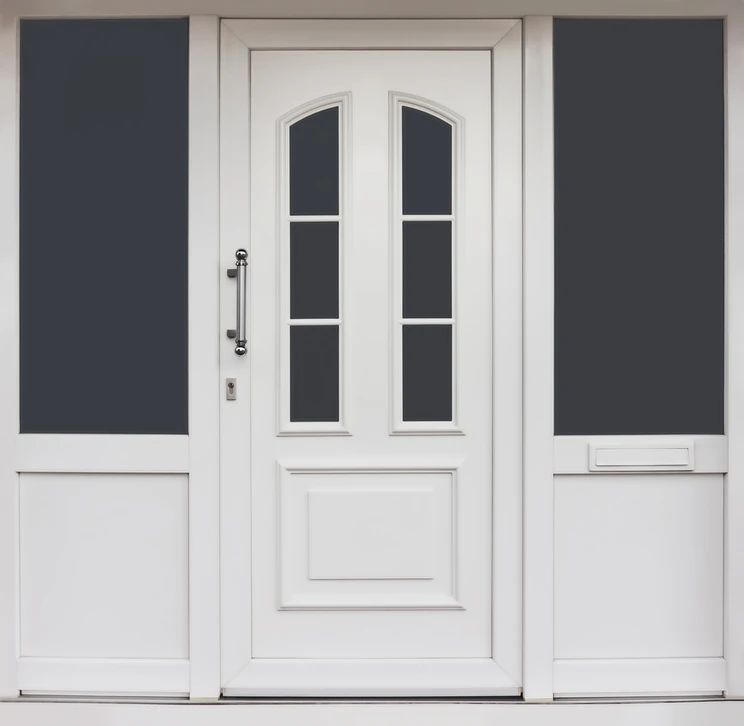 Photographie d'une porte d'entrée PVC moderne gris anthracite ou blanche avec vitrages, installée dans l'entrée d'une maison contemporaine. La porte est fermée, vue de face, légèrement de trois-quarts pour montrer sa structure. L'entrée autour montre des murs peints, un léger aménagement résidentiel sobre et soigné. La porte doit apparaître sécurisée, élégante et confortable, sans personne ni texte visible.